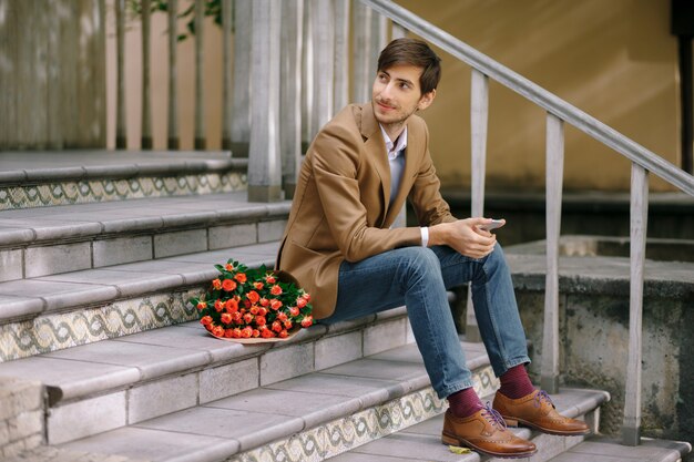 Uomo bello con il telefono e il mazzo di rose