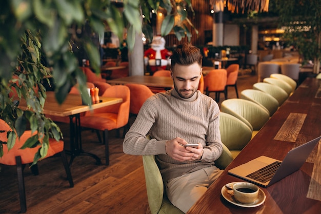 Uomo bello di affari che lavora al computer e che beve caffè in un caffè