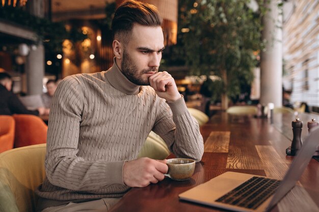 Uomo bello di affari che lavora al computer e che beve caffè in un caffè