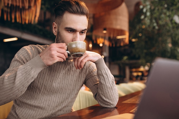 Uomo bello di affari che lavora al computer e che beve caffè in un caffè