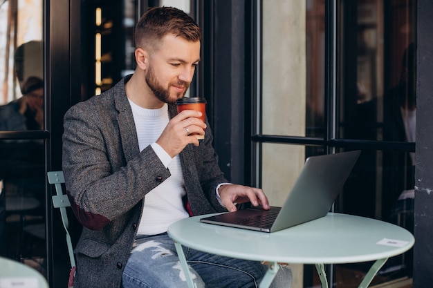 Uomo bello di affari che lavora al computer portatile in caffè