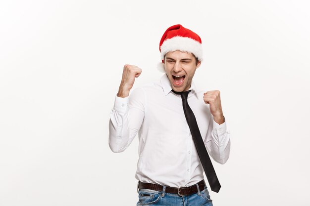 Uomo bello di affari che porta il cappello della Santa che posa con l'espressione facciale sorprendente su bianco.