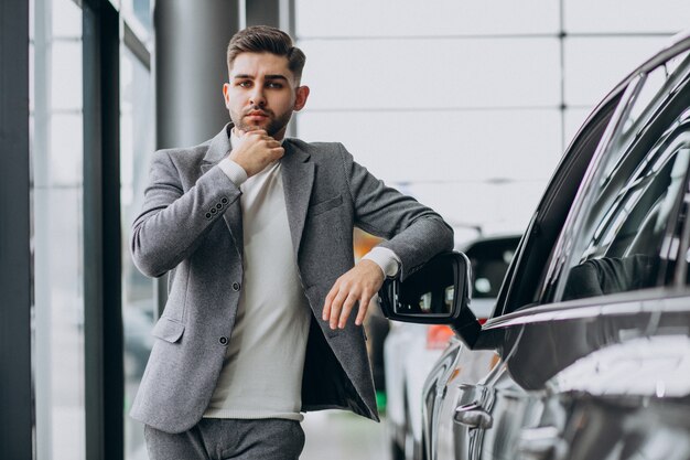 Uomo bello di affari che sceglie un'automobile in una sala d'esposizione dell'automobile