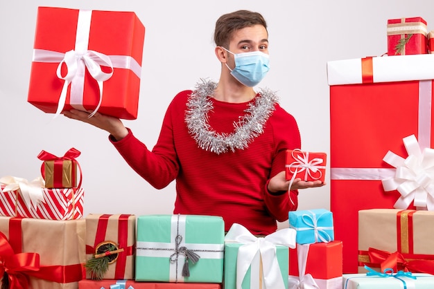 Uomo bello di vista frontale con la maschera che si siede intorno ai regali di natale