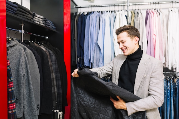 Uomo bello felice che esamina giacca nel negozio di vestiti