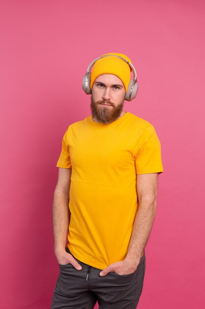 Uomo bello in ascolto casuale di musica con le cuffie isolato su sfondo rosa