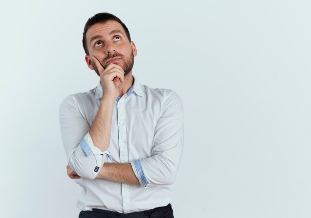 Uomo bello premuroso mette la mano sul mento alzando lo sguardo isolato sul muro bianco