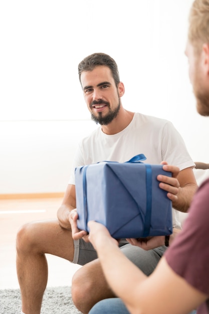 Uomo bello sorridente che cattura il contenitore di regalo spostato blu dal suo amico