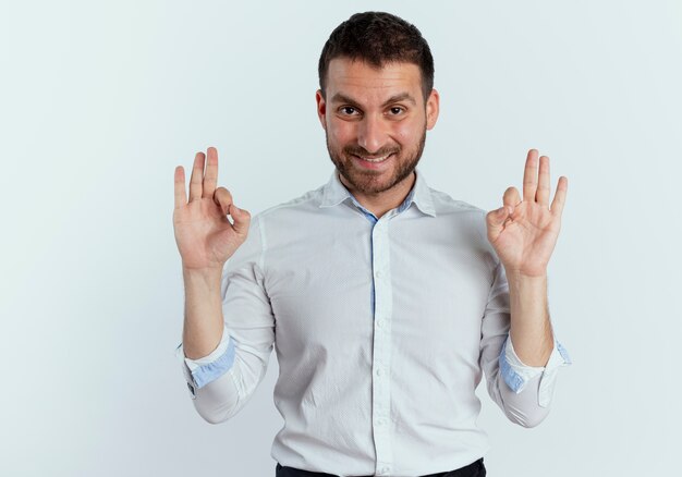 Uomo bello sorridente gesti il segno giusto della mano isolato sul muro bianco