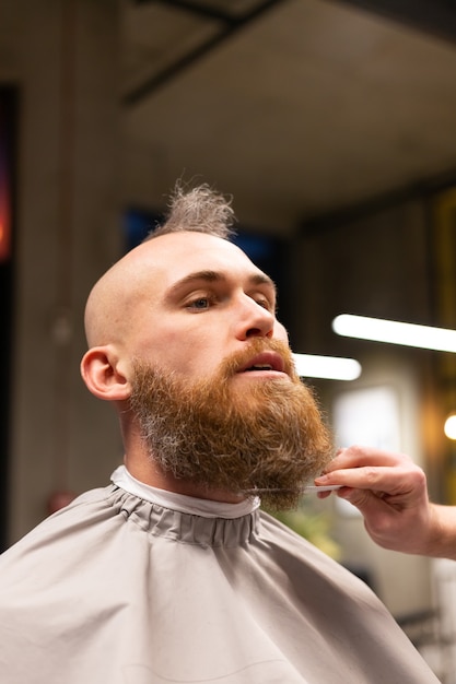 Uomo brutale europeo con una barba tagliata in un negozio di barbiere