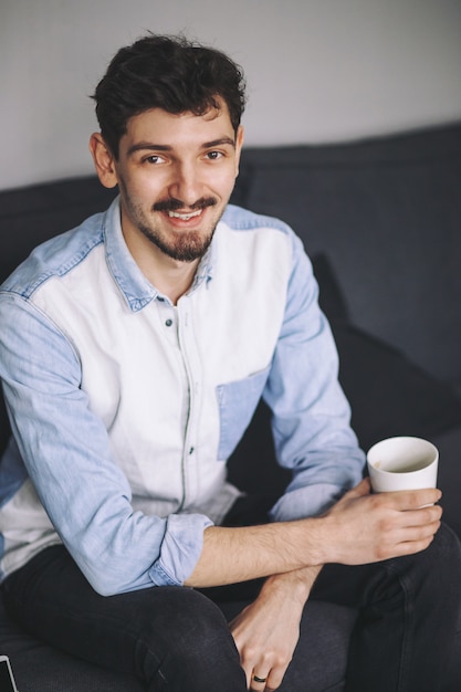 Uomo casuale bello che si siede sullo strato che mangia caffè