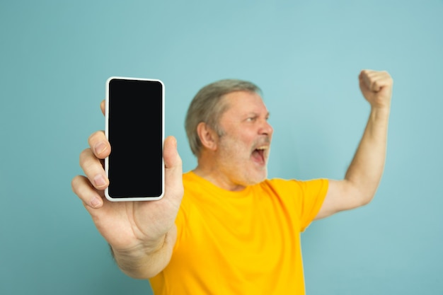 Uomo caucasico che mostra lo schermo in bianco del telefono sull'azzurro