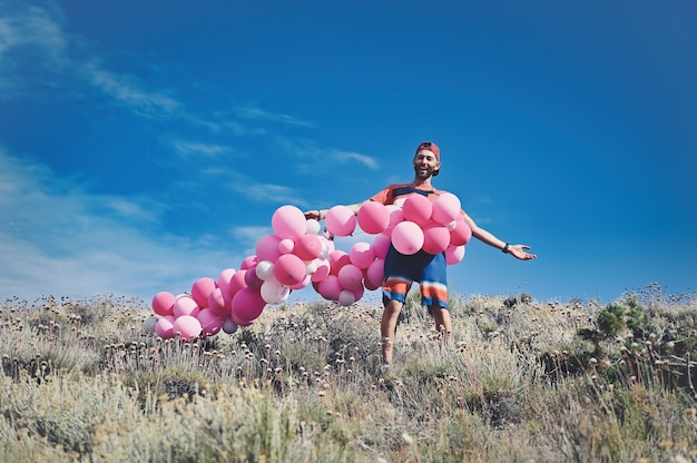 Uomo caucasico circondato da una serie di palloncini rosa mentre si trova su una montagna