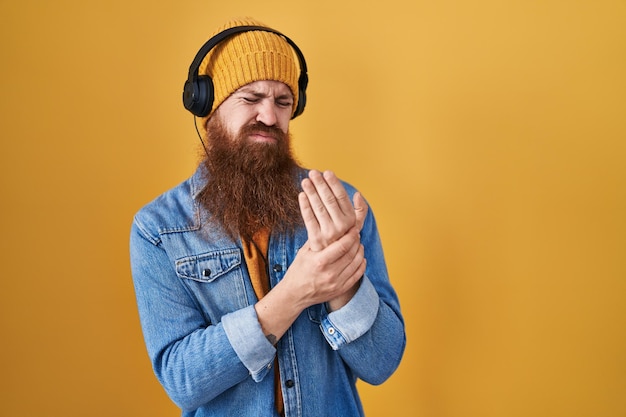 Uomo caucasico con barba lunga che ascolta musica utilizzando le cuffie che soffrono di dolore alle mani e alle dita artrite infiammazione