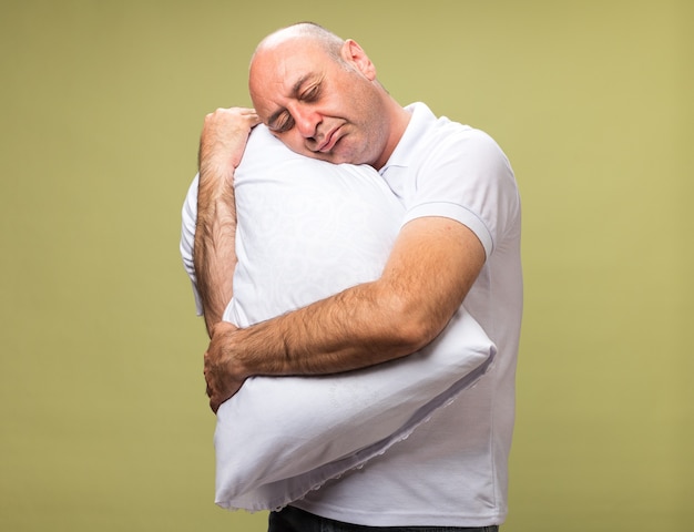 uomo caucasico malato adulto assonnato che tiene e che mette la testa sul cuscino isolato sulla parete verde oliva con lo spazio della copia