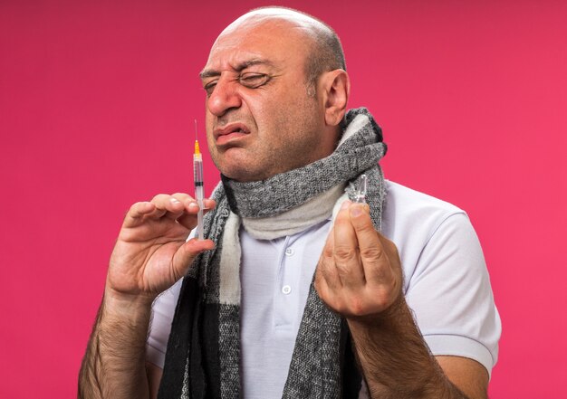 Uomo caucasico malato adulto dispiaciuto con sciarpa intorno al collo che tiene la fiala e la siringa da fiuto isolata sulla parete rosa con lo spazio della copia