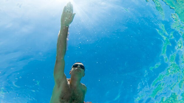 Uomo caucasico nuotare sott'acqua in occhiali da nuoto blu acqua trasparente