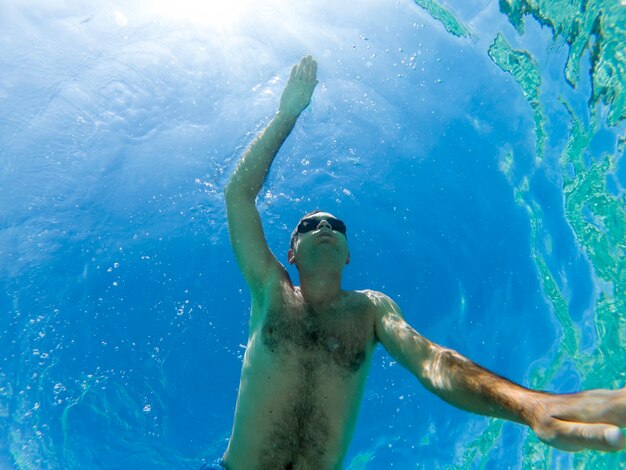 Uomo caucasico nuotare sott'acqua in occhiali da nuoto blu acqua trasparente