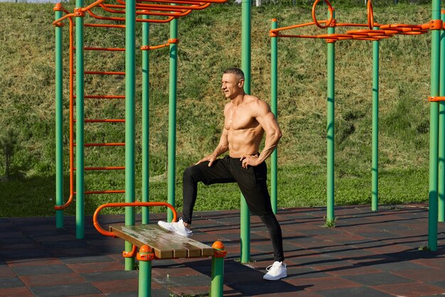 Uomo caucasico sportivo che allunga le gambe sulla panchina all'aperto