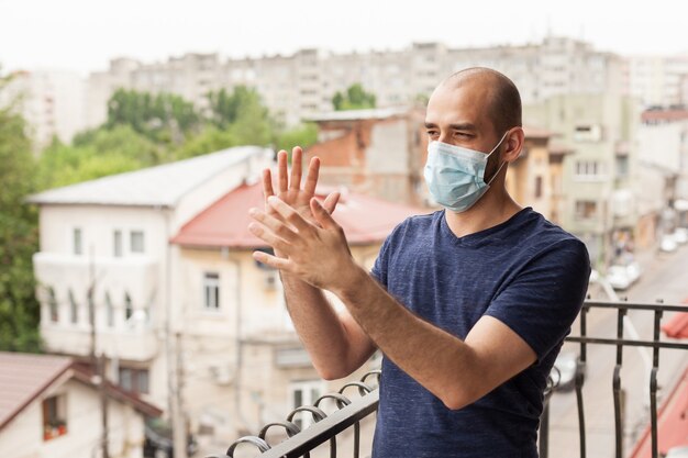 Uomo che applaude sul suo balcone per supportare il personale medico durante la pandemia globale.
