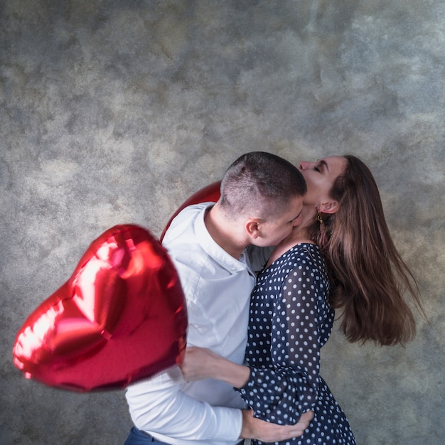 Uomo che bacia la donna con palloncini cuore