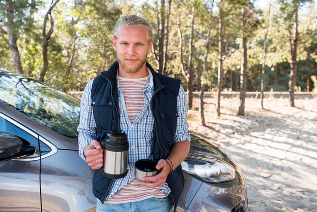 Uomo che beve caffè e seduto accanto alla macchina