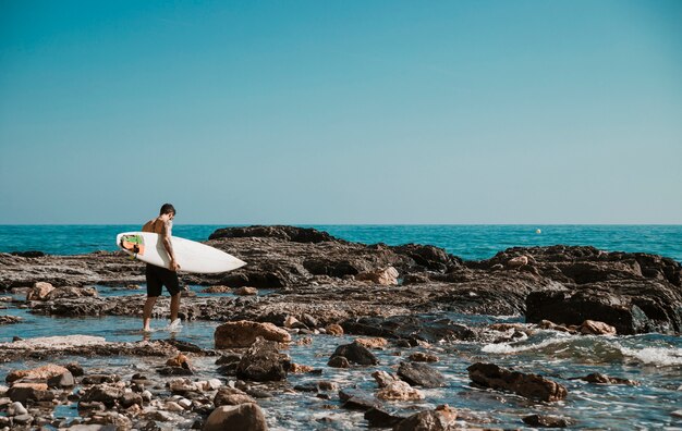 Uomo che cammina sulla riva del mare con tavola da surf