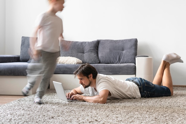 Uomo che cerca di lavorare su un laptop da casa mentre i suoi figli corrono in giro