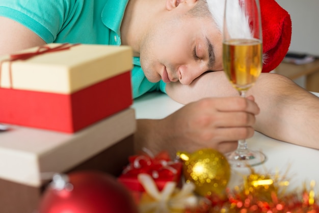 Uomo che dorme sul tavolo con regali di Natale e bicchiere di champagne