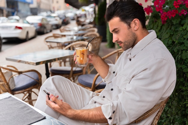 Uomo che fa una pausa caffè ghiacciata mentre utilizza lo smartphone