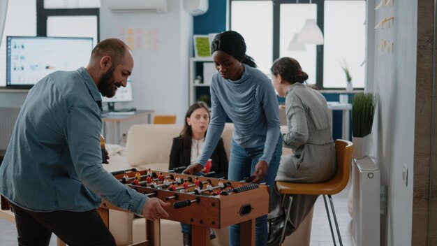 Uomo che gioca a calcio con una donna al biliardino, incontro per un drink e intrattenimento in ufficio dopo il lavoro. Gruppo multietnico di colleghi che si godono birra e pizza dopo l'orario di lavoro