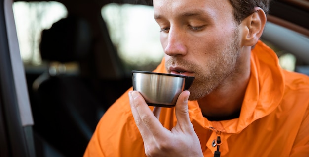 Uomo che gode di una bevanda calda durante un viaggio in auto