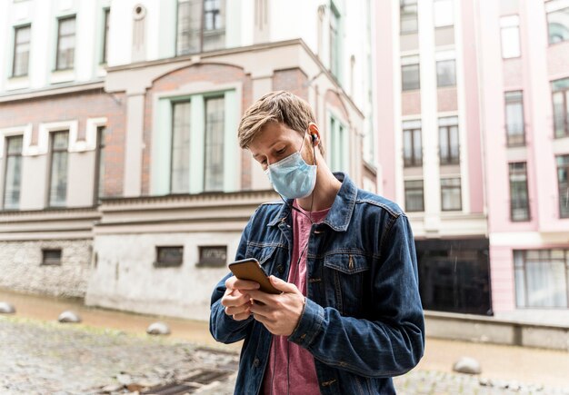 Uomo che guarda attraverso il suo telefono mentre indossa una maschera medica con spazio di copia
