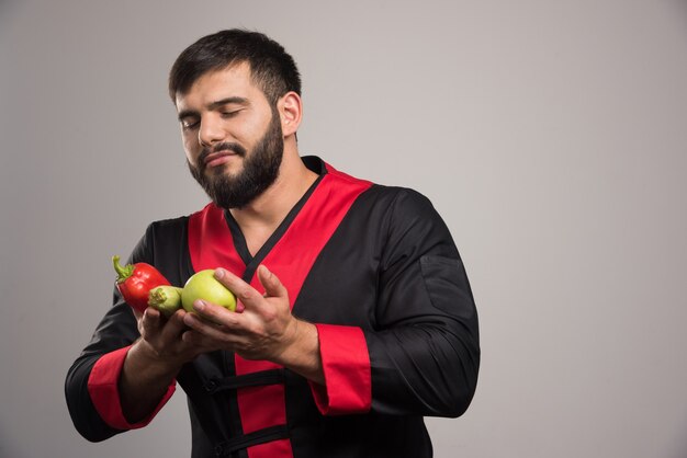 Uomo che guarda il peperone rosso, la mela e le zucchine.