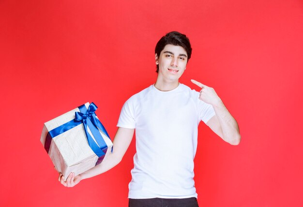 Uomo che indica la sua confezione regalo bianca con nastro blu