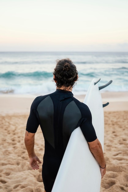 Uomo che indossa abiti da surfista che cammina sulla sabbia