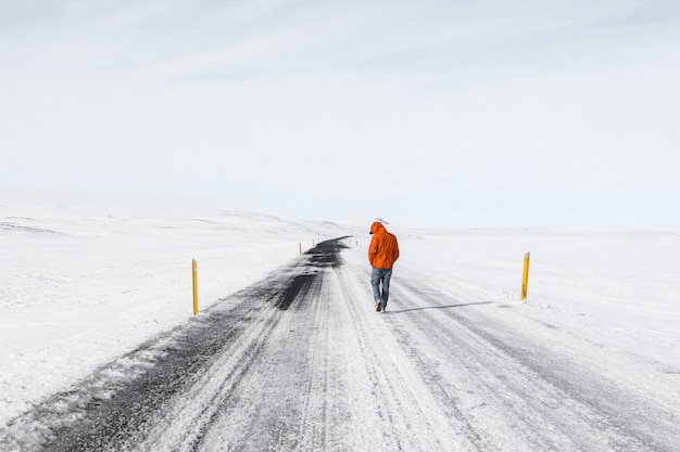 uomo che indossa giacca arancione camminando lungo una strada statale innevata
