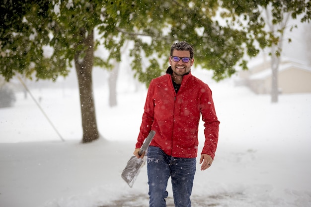 Uomo che indossa una giacca rossa e cammina in un campo innevato mentre si tiene la pala da neve