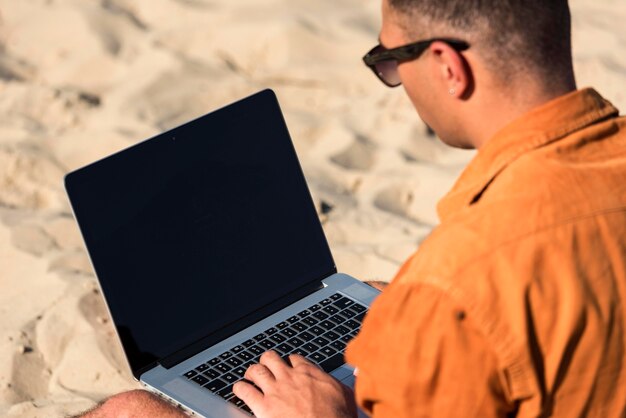 Uomo che lavora al computer portatile in spiaggia