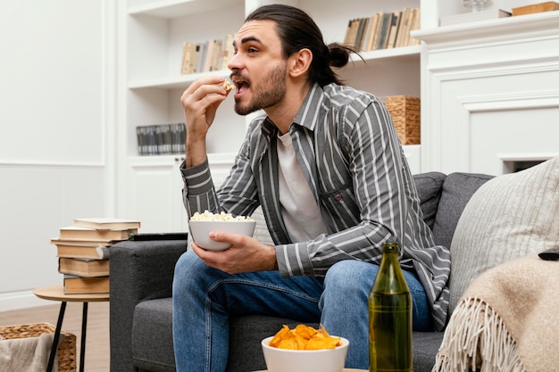 Uomo che mangia popcorn e guarda la tv sul divano