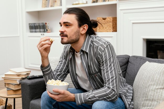 Uomo che mangia popcorn e guarda la tv sul divano