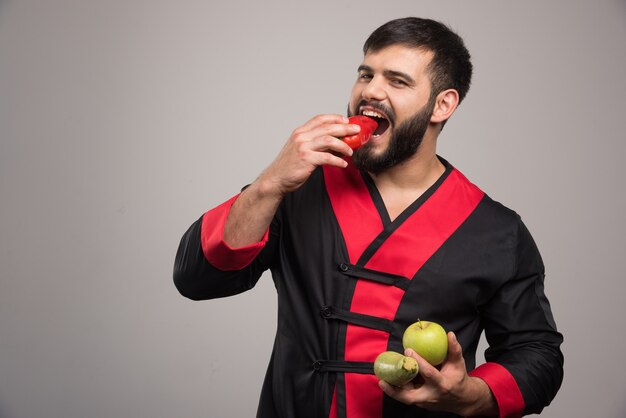 Uomo che mangia un peperone rosso e che tiene la mela con le zucchine.