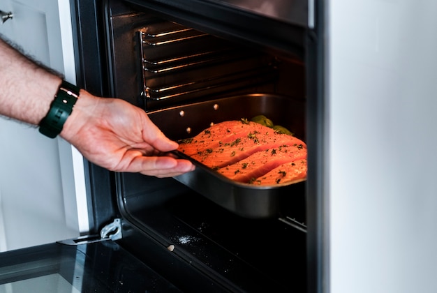 Uomo che mette la bistecca di salmone crudo nel forno