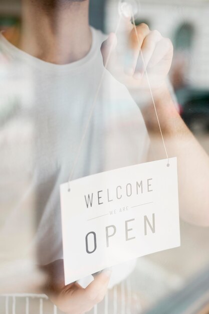 Uomo che mette su segno aperto sulla finestra della caffetteria