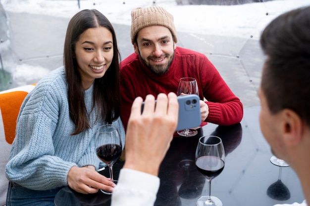 Uomo che mostra lo schermo dello smartphone agli amici mentre beve vino durante la riunione