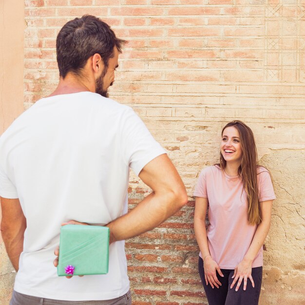 Uomo che nasconde il regalo dalla sua ragazza felice alle spalle