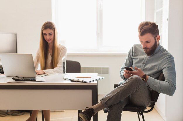 Uomo che naviga smartphone vicino alla donna lavoratrice