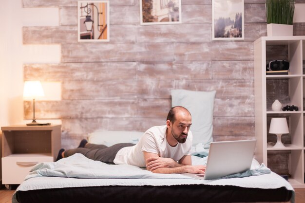 Uomo che naviga sul portatile di notte a letto con indosso un pigiama.