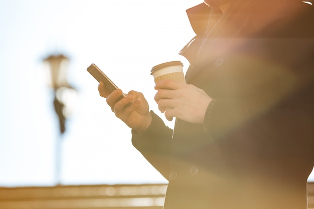 Uomo che per mezzo del telefono cellulare e bevendo caffè all'aperto nel giorno soleggiato