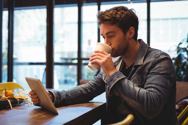 Uomo che per mezzo della compressa digitale mentre mangiando caffè